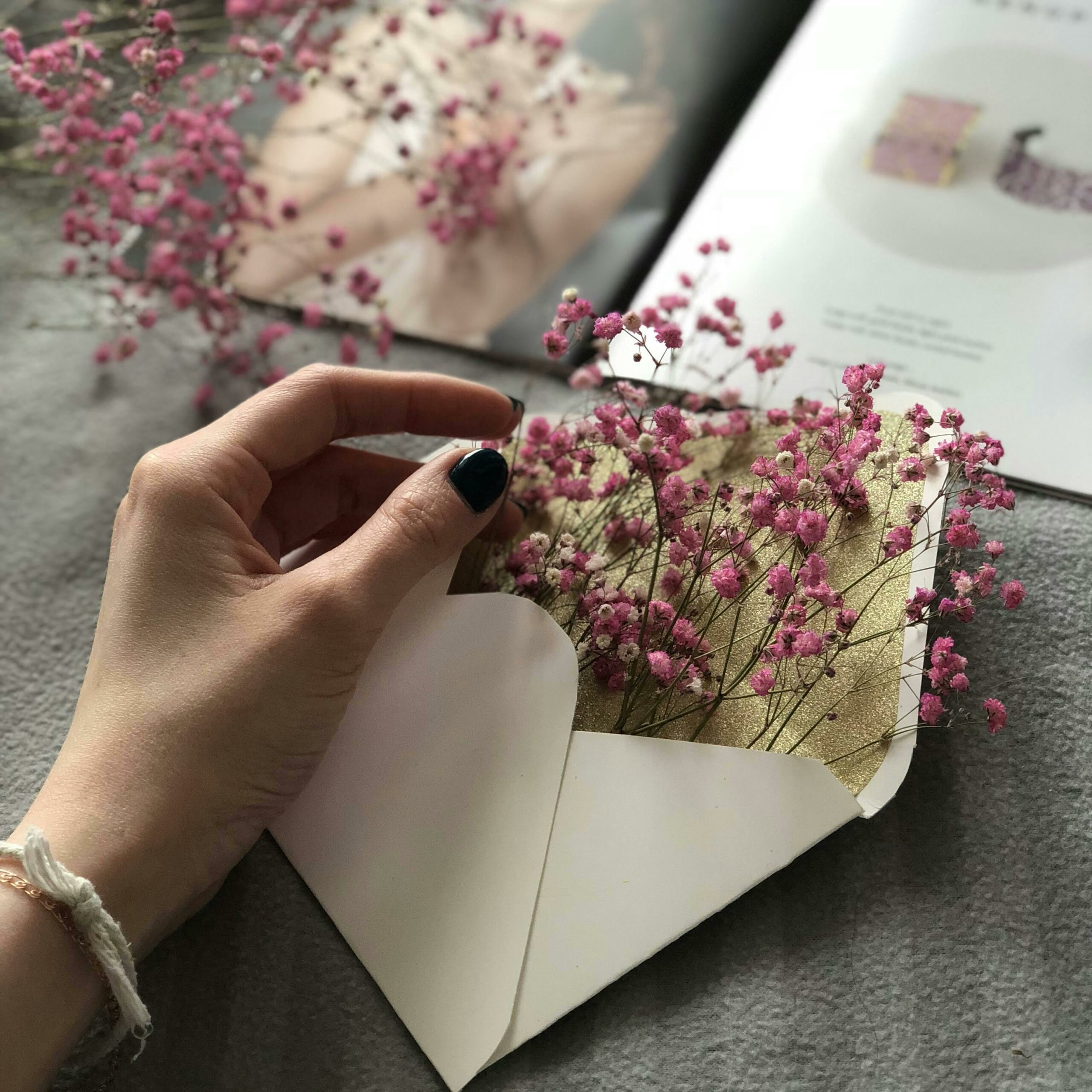 A delicate hand holds a white envelope with pink flowers inside, adding an artistic touch.