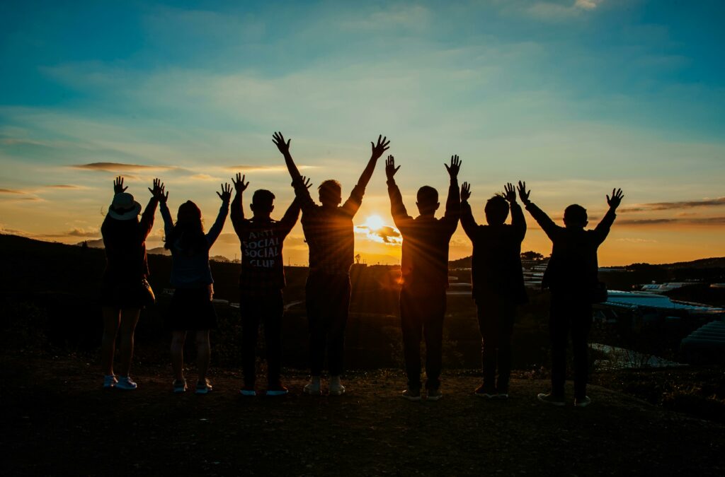 Un groupe diversifié d'amis lève les bras en signe de célébration devant un coucher de soleil vibrant en toile de fond.